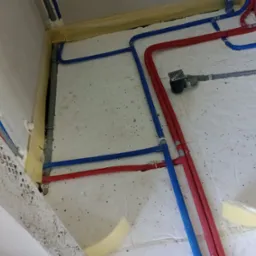 Podłogowe rozprowadzenie instalacji wodnej i grzewczej z rur PEX w kolorze niebieskim i czerwonym, widoczny odpływ liniowy, izolacja termiczna przy ścianach.