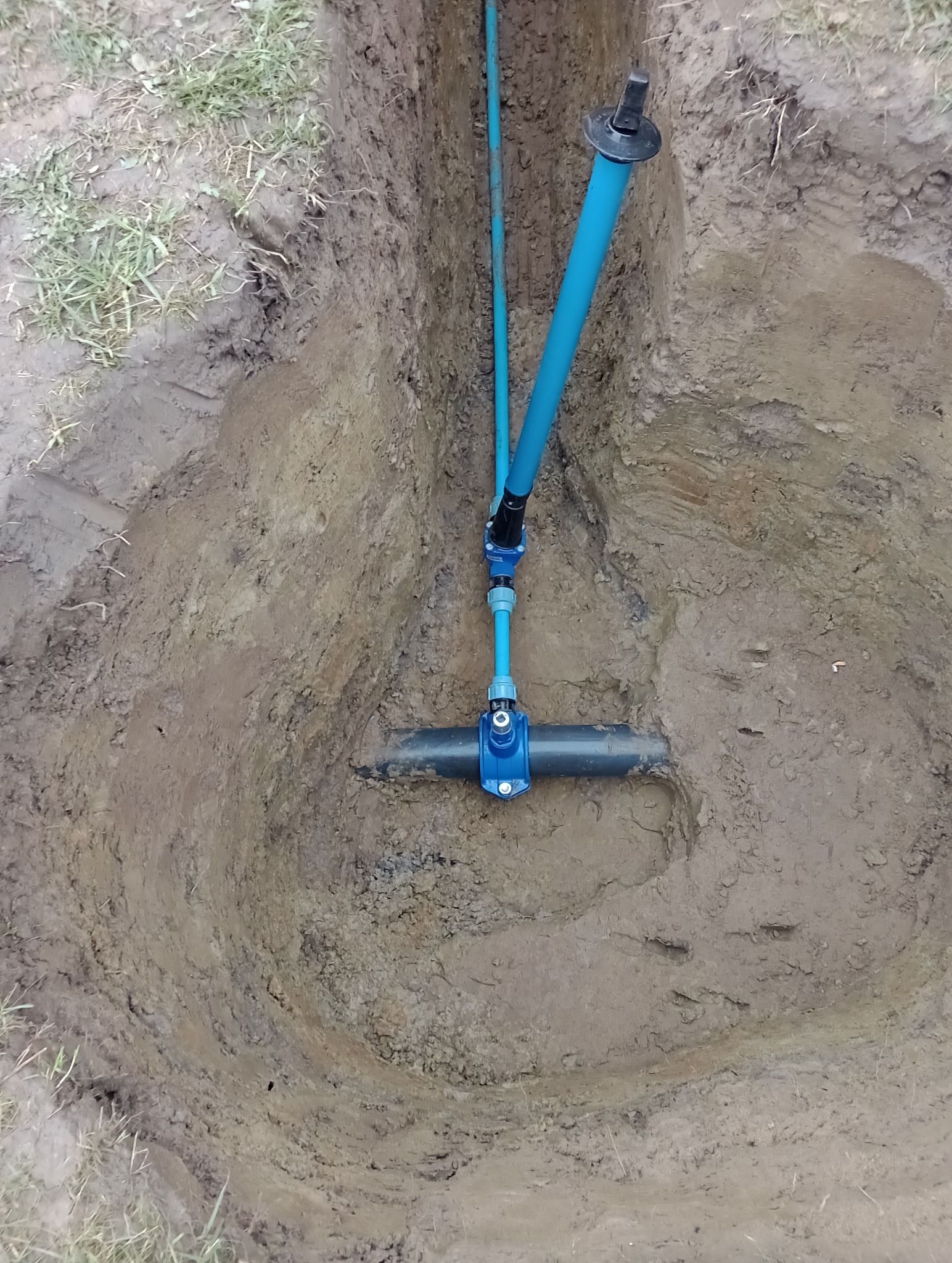 Niebieskie rury wodociągowe z łącznikami w wykopie ziemnym, widok z góry.