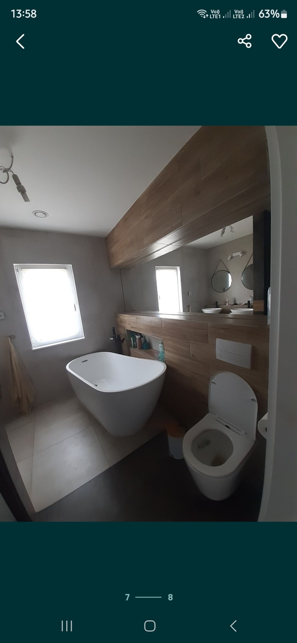 Nowoczesna łazienka z wolnostojącą wanną, toaletą, umywalkami i drewnianymi akcentami na ścianie, widok z szerokiego kąta.