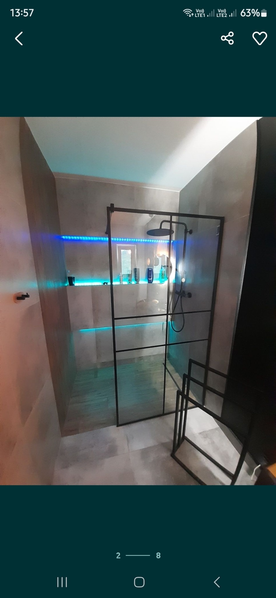 Nowoczesna kabina prysznicowa typu walk-in z czarnymi profilami, oświetleniem LED w kolorze niebieskim, szarymi płytkami i minimalistycznym wieszakiem na ręczniki.