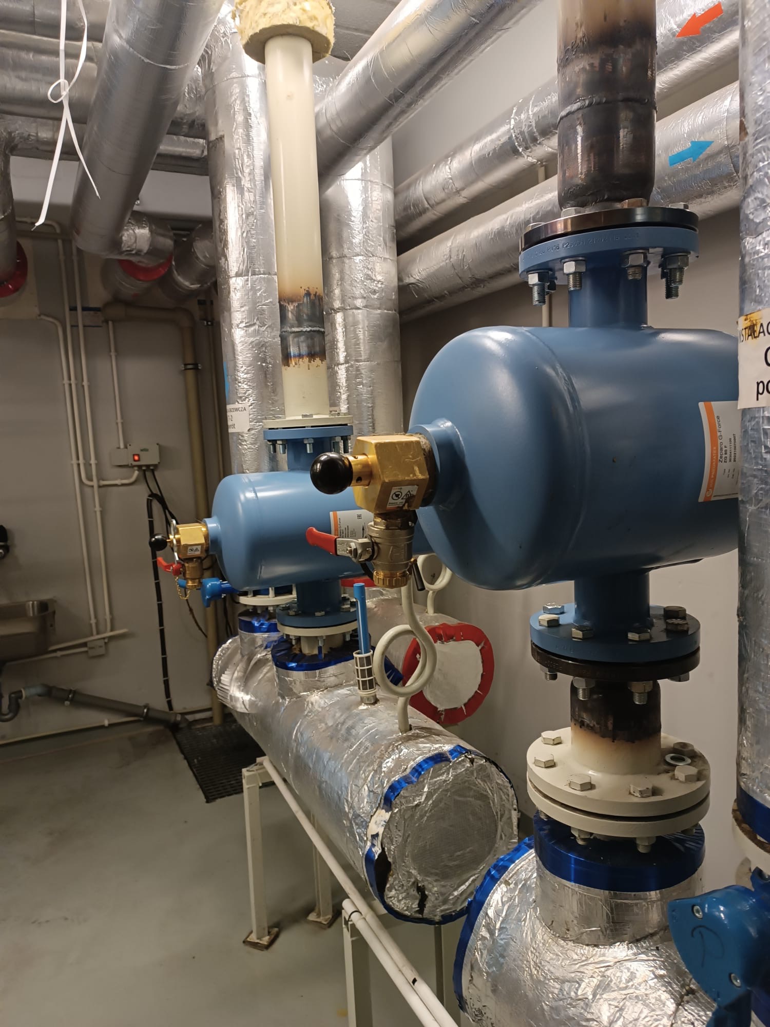 Błękitne filtry na rurach z izolacją aluminiową, część instalacji w pomieszczeniu technicznym. Widoczne zawory i elementy złączne. Instalacja po montażu.