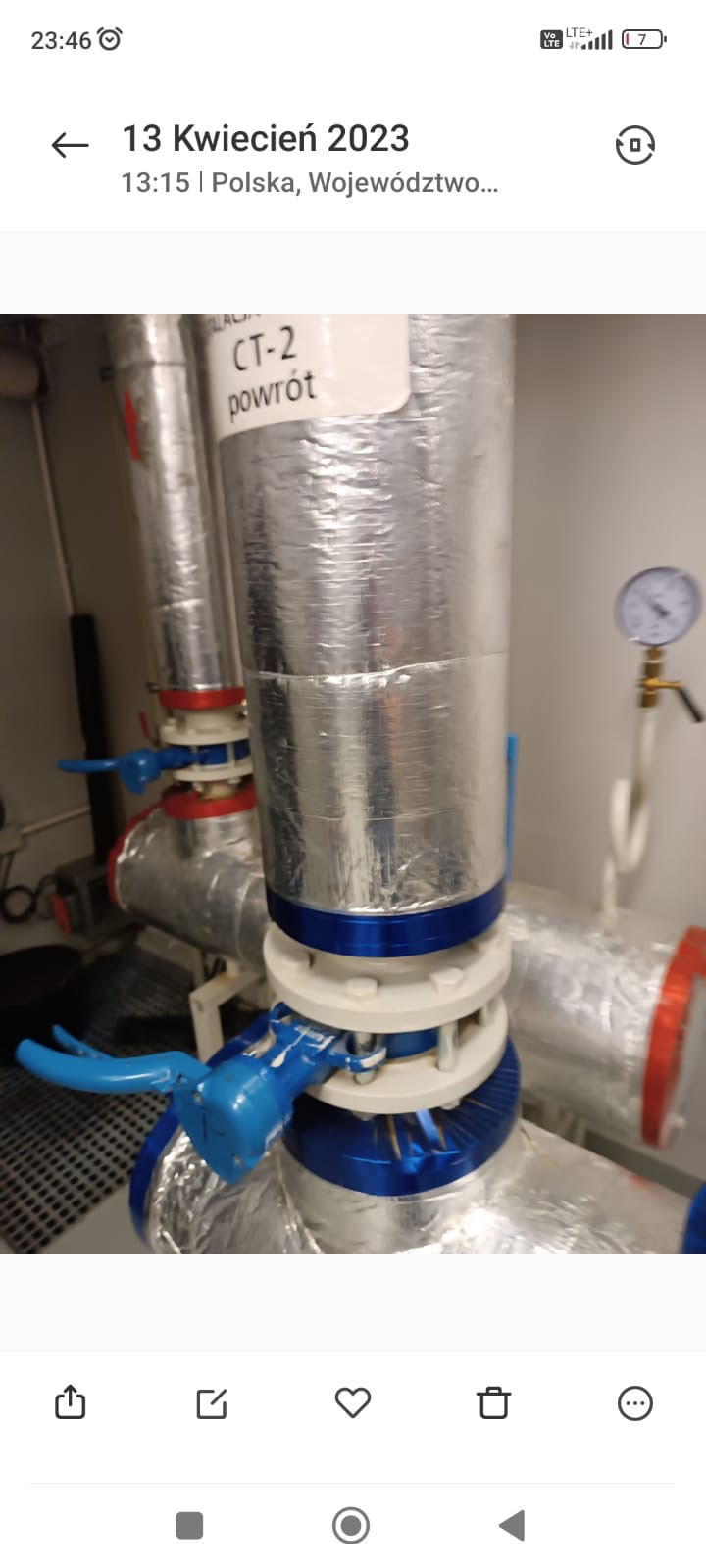 Izolowane rury z zaworami i manometrem w kotłowni, etykieta 'CT-2 powrót'. Instalacja grzewcza w pomieszczeniu technicznym.