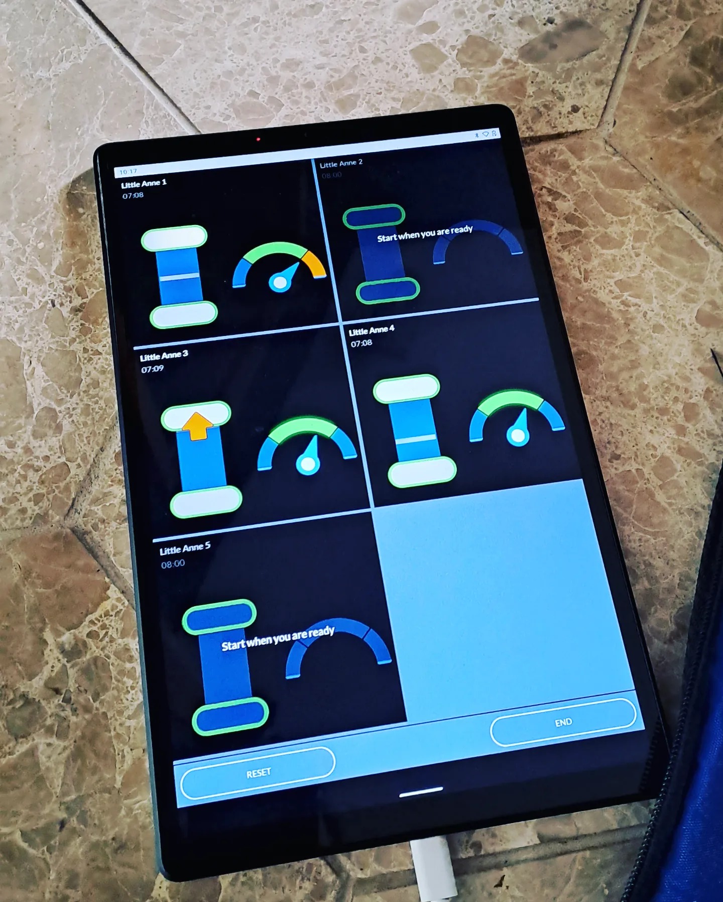 Tablet wyświetlający interfejs aplikacji do monitorowania i oceny ćwiczeń resuscytacyjnych na fantomach Little Anne, z widocznymi wskaźnikami postępu i instrukcjami.