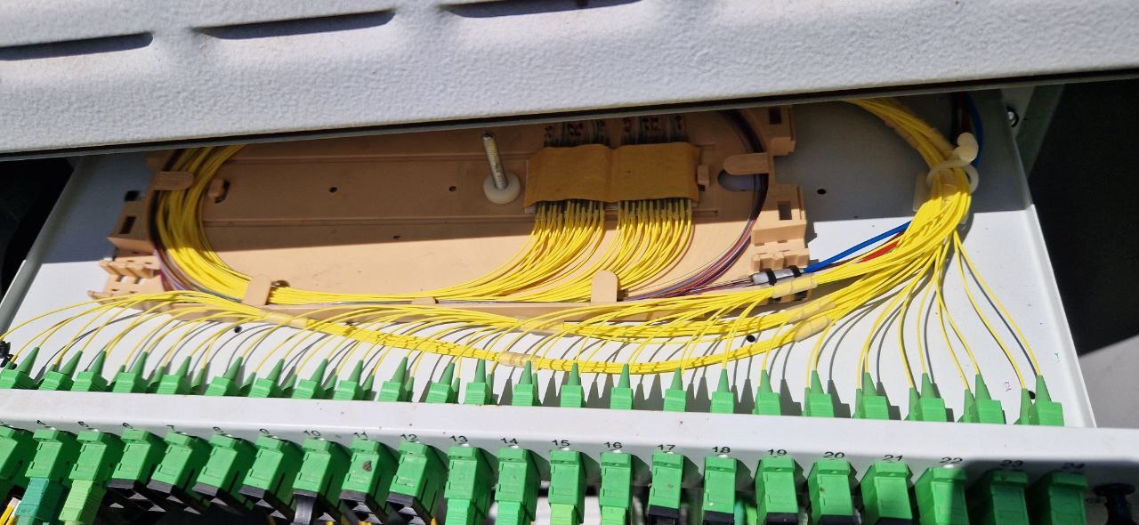 Rozdzielnica światłowodowa z precyzyjnie ułożonymi żółtymi kablami światłowodowymi i zielonymi złączkami, widoczne numerowane porty.