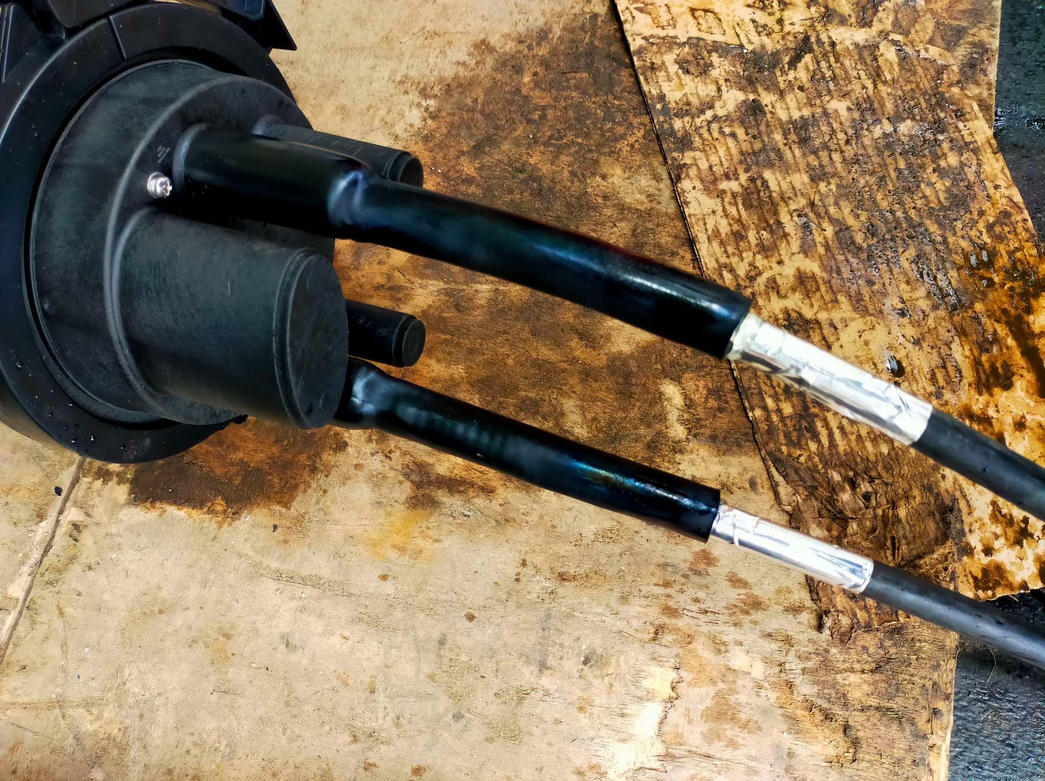 Złącze światłowodowe z dwoma kablami zabezpieczonymi taśmą aluminiową, umieszczone na brudnej, drewnianej powierzchni.