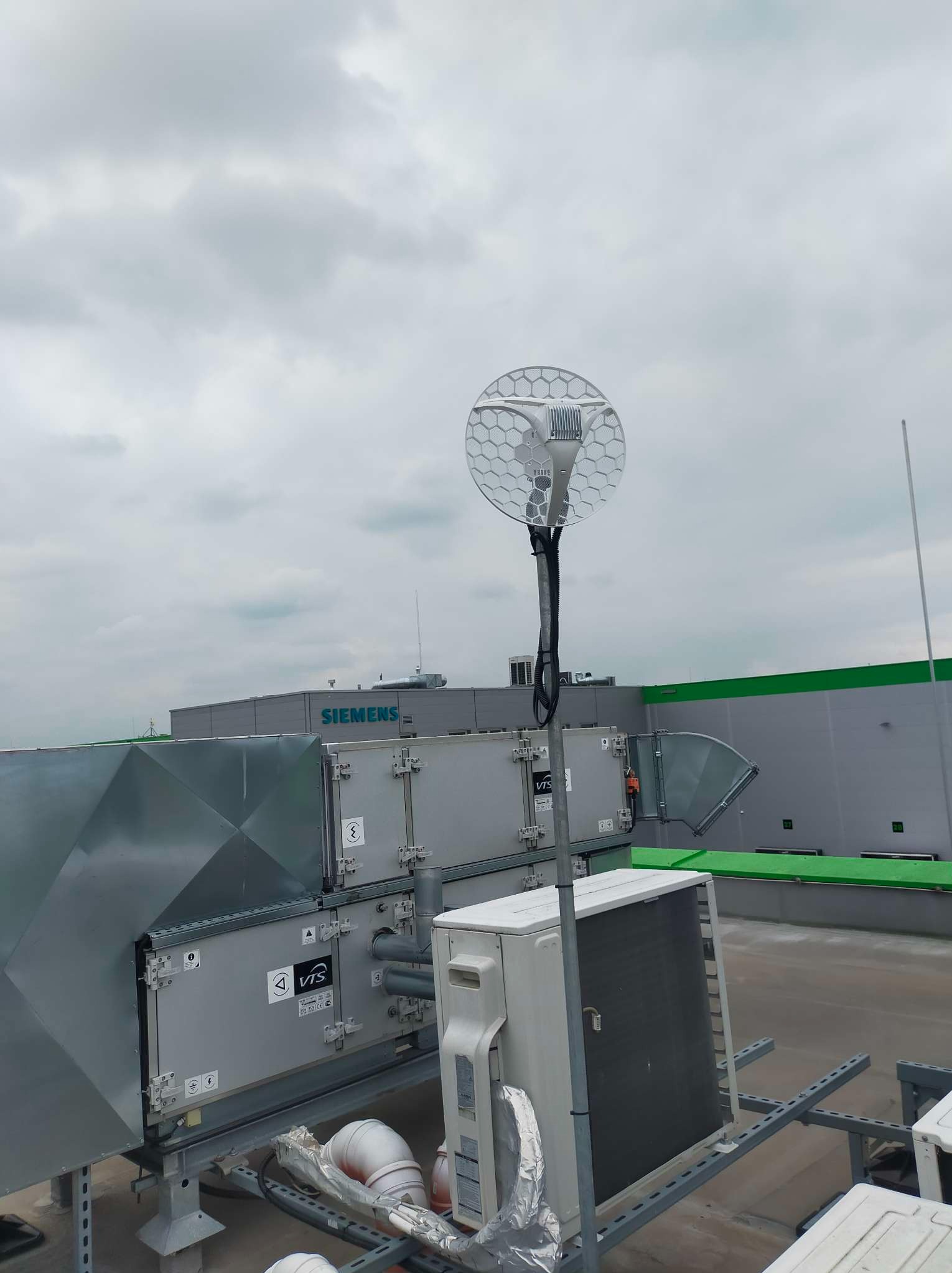 Antena telekomunikacyjna o strukturze plastra miodu zamontowana na dachu budynku przemysłowego, w tle widoczne instalacje wentylacyjne i klimatyzacyjne oraz logo Siemens