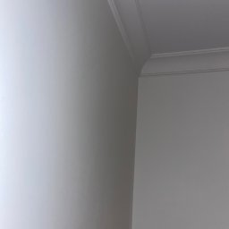 RJ Build - Fragment pomalowanego na biało narożnika pokoju z dekoracyjnym wykończeniem sufitu.