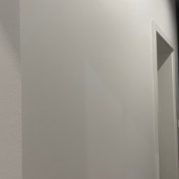 RJ Build - Fragment ściany po zakończonym malowaniu na kolor biały, widoczna ościeżnica drzwiowa.