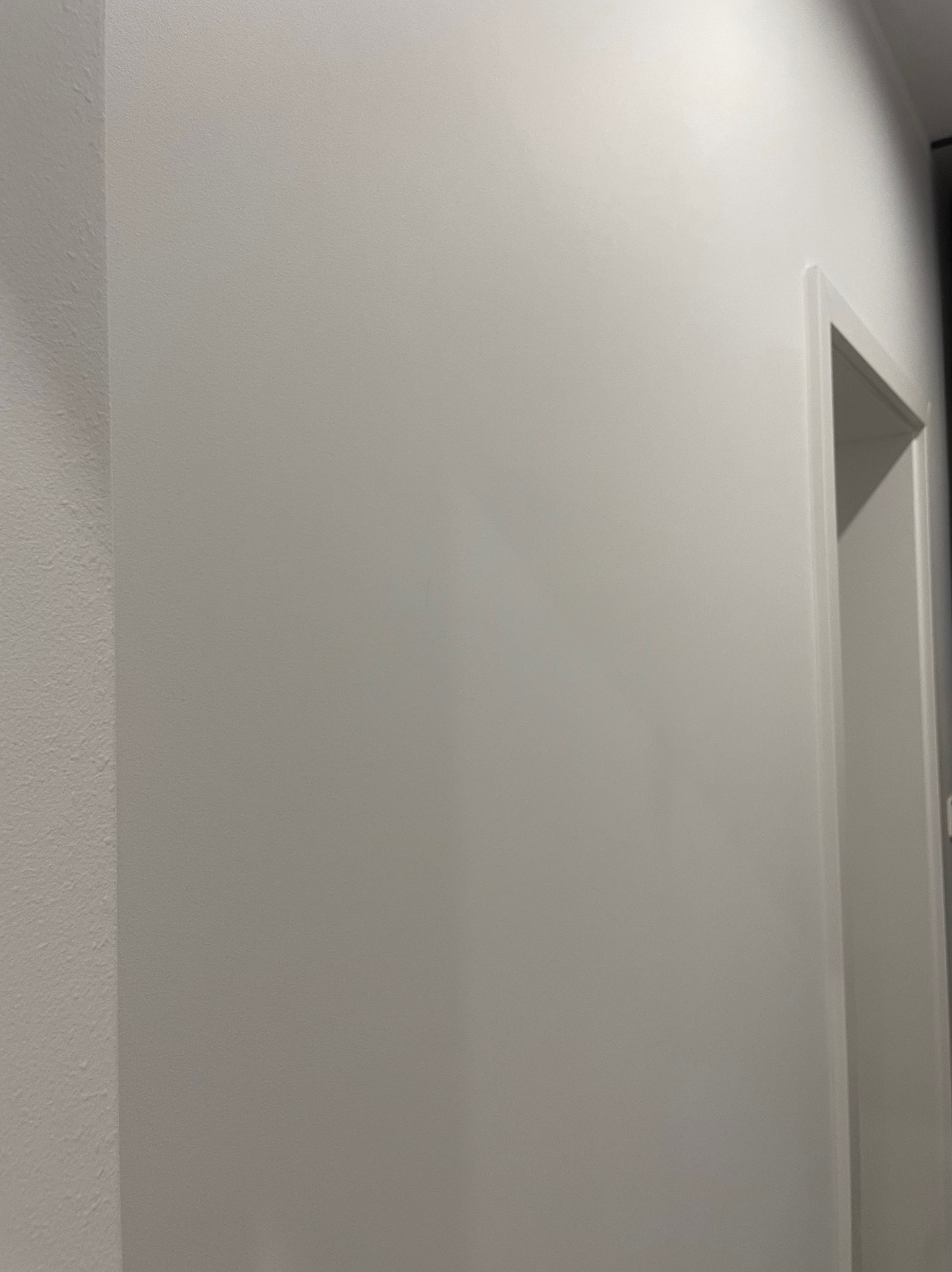 Fragment ściany po zakończonym malowaniu na kolor biały, widoczna ościeżnica drzwiowa.