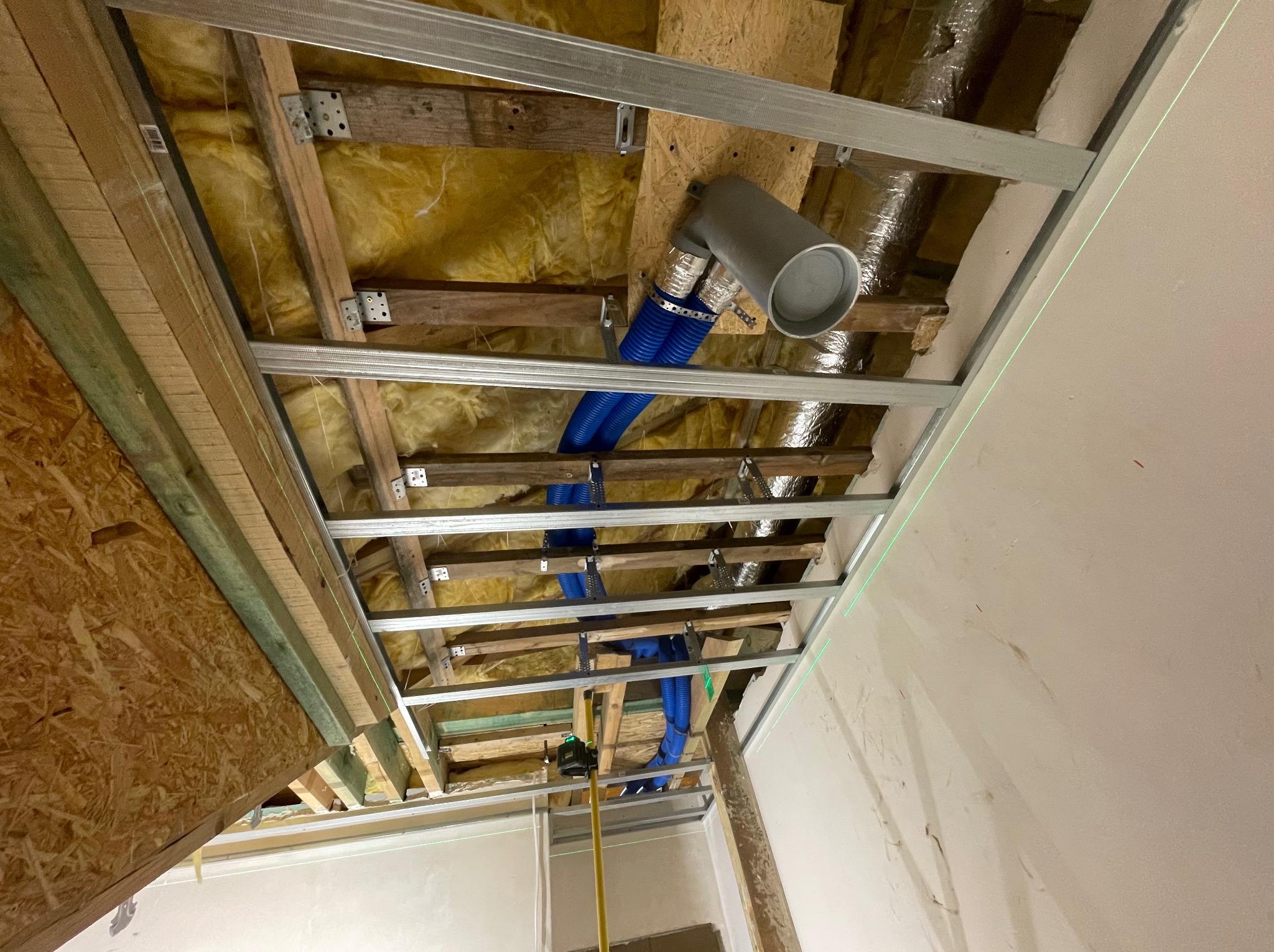 Sufit podwieszany w trakcie montażu w Szczecinie, widoczne profile, izolacja, rury wentylacyjne i laserowy niwelator wyznaczający poziom.