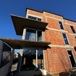 Prim - Budynek w trakcie budowy z widocznymi elementami konstrukcyjnymi tarasu lub balkonu i niezadaszoną przestrzenią.