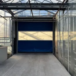 Brama segmentowa w hali magazynowej, z widoczną konstrukcją stalową i przeszkleniami w dachu. Brama w kolorze niebieskim z jasnym pasem na środku.