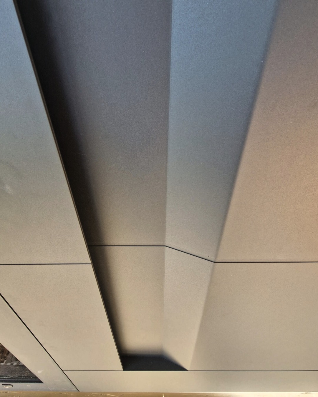 Nowoczesna zabudowa balkonu z szarych paneli, widok od spodu. Geometryczny wzór, precyzyjne łączenia, minimalistyczny design. Wykończenie w matowym odcieniu szarości.