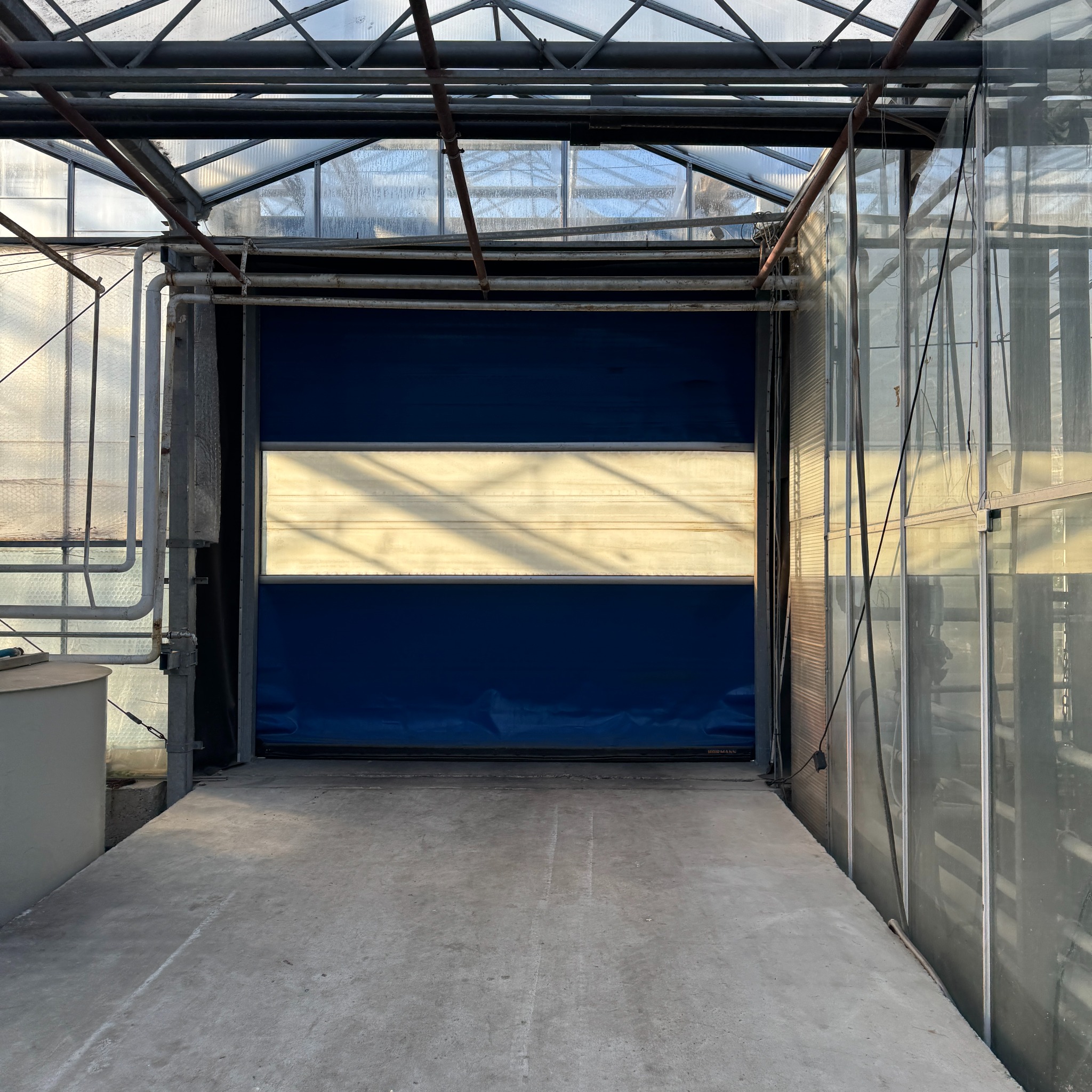 Brama segmentowa w hali magazynowej, z widoczną konstrukcją stalową i przeszkleniami w dachu. Brama w kolorze niebieskim z jasnym pasem na środku.