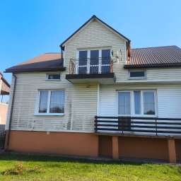 Polska Grupa Termomodernizacyjna - Dom z sidingiem i balkonem, widoczne ślady zabrudzeń na elewacji, brązowy dach i podmurówka. Na ścianie numer domu '50'.