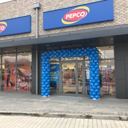 PB Ciastowicz sp. z o.o. - Wejście do sklepu Pepco ozdobione łukiem z niebieskich balonów, szyldy z logo Pepco nad wejściem, osoba z laską przechodząca obok.