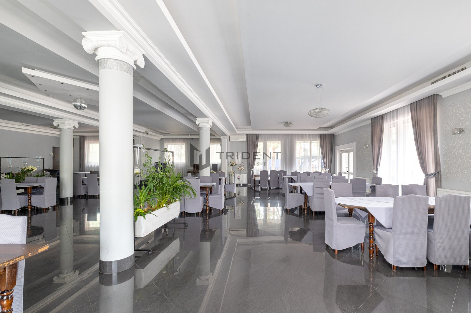 Eleganckie wnętrze sali bankietowej z kolumnami, lustrzaną podłogą i nakrytymi stołami w odcieniach szarości.