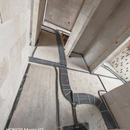 Volt-Elektro Szymon Osiurek - Szare rury instalacji elektrycznej, zabezpieczone białymi opaskami, prowadzone po ścianach i suficie surowego wnętrza w trakcie budowy.