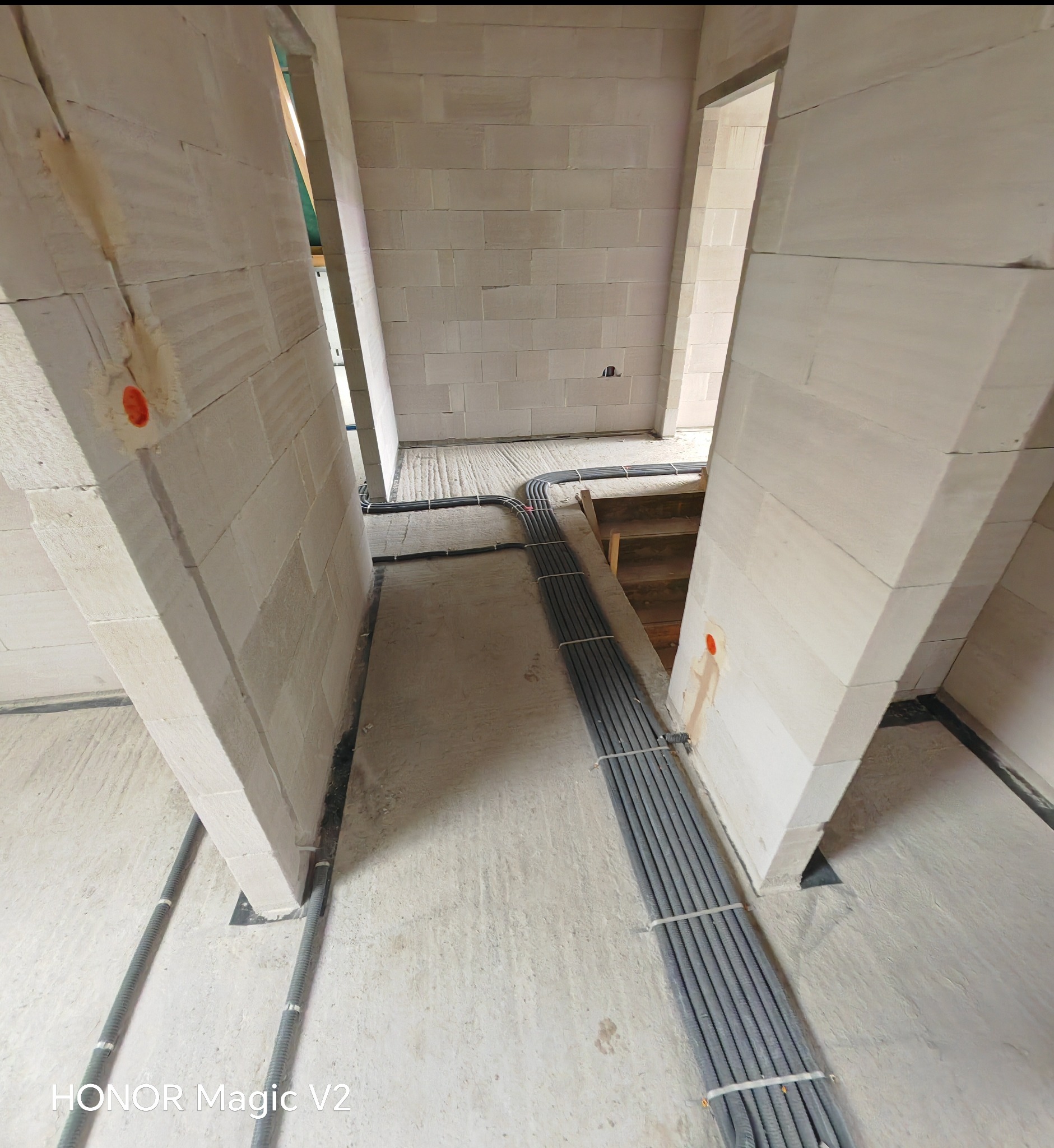 Szare rury w korytach, zabezpieczone białymi opaskami, prowadzone w surowym wnętrzu budynku z białych pustaków, przed wylaniem posadzki.