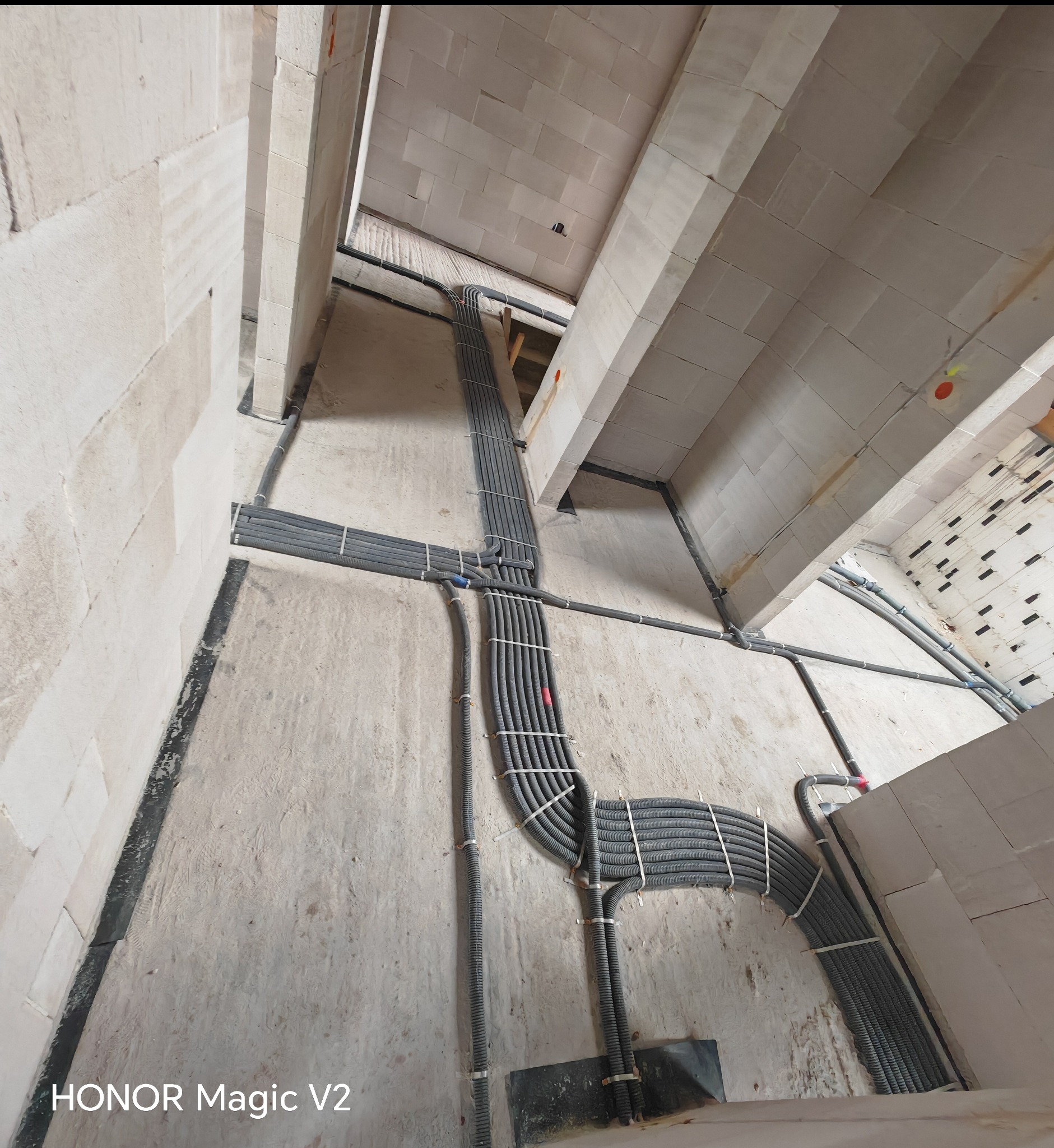 Szare rury instalacji elektrycznej, zabezpieczone białymi opaskami, prowadzone po ścianach i suficie surowego wnętrza w trakcie budowy.