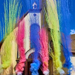 FOTOFRAJDA ALEKSANDRA MICEK - Para młoda przed kościołem, otoczona kolorowymi strumieniami dymu, tworzącymi efektowną oprawę uroczystości.