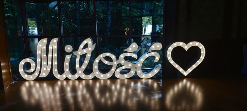 Świecący napis 'Miłość' i serce z żarówkami jako dekoracja sali weselnej, widok z niskiej perspektywy.