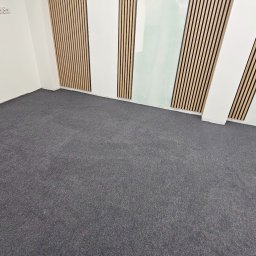 Perfect Floor Paweł Wojciechowicz - Szara wykładzina dywanowa w pokoju z panelami ściennymi z drewna. Widok na całą podłogę, świeżo po montażu. Minimalistyczne wnętrze.