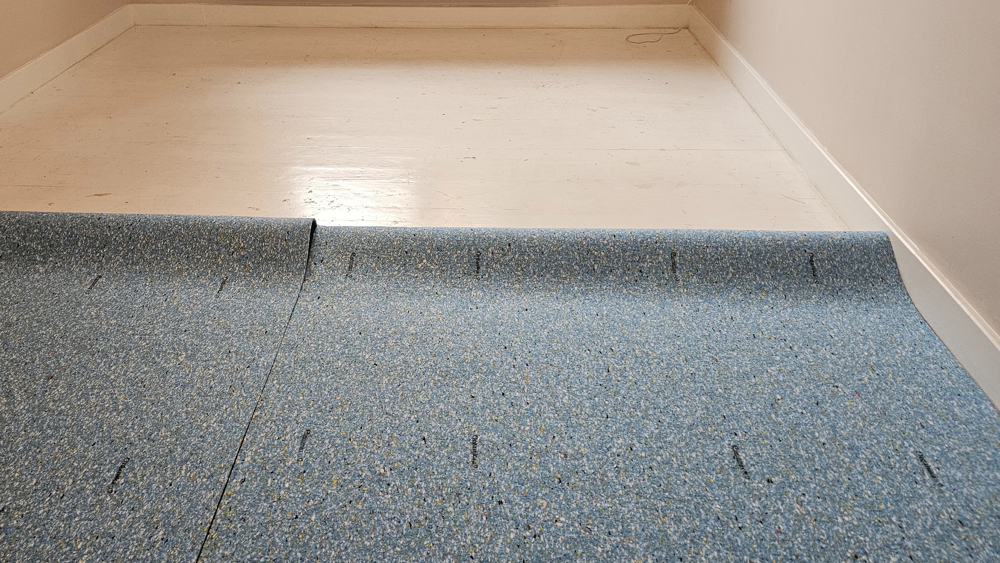 Niebieska wykładzina dywanowa z rolki, częściowo rozłożona na podłodze w Bolesławcu. Widoczny fragment podłogi przed położeniem wykładziny.