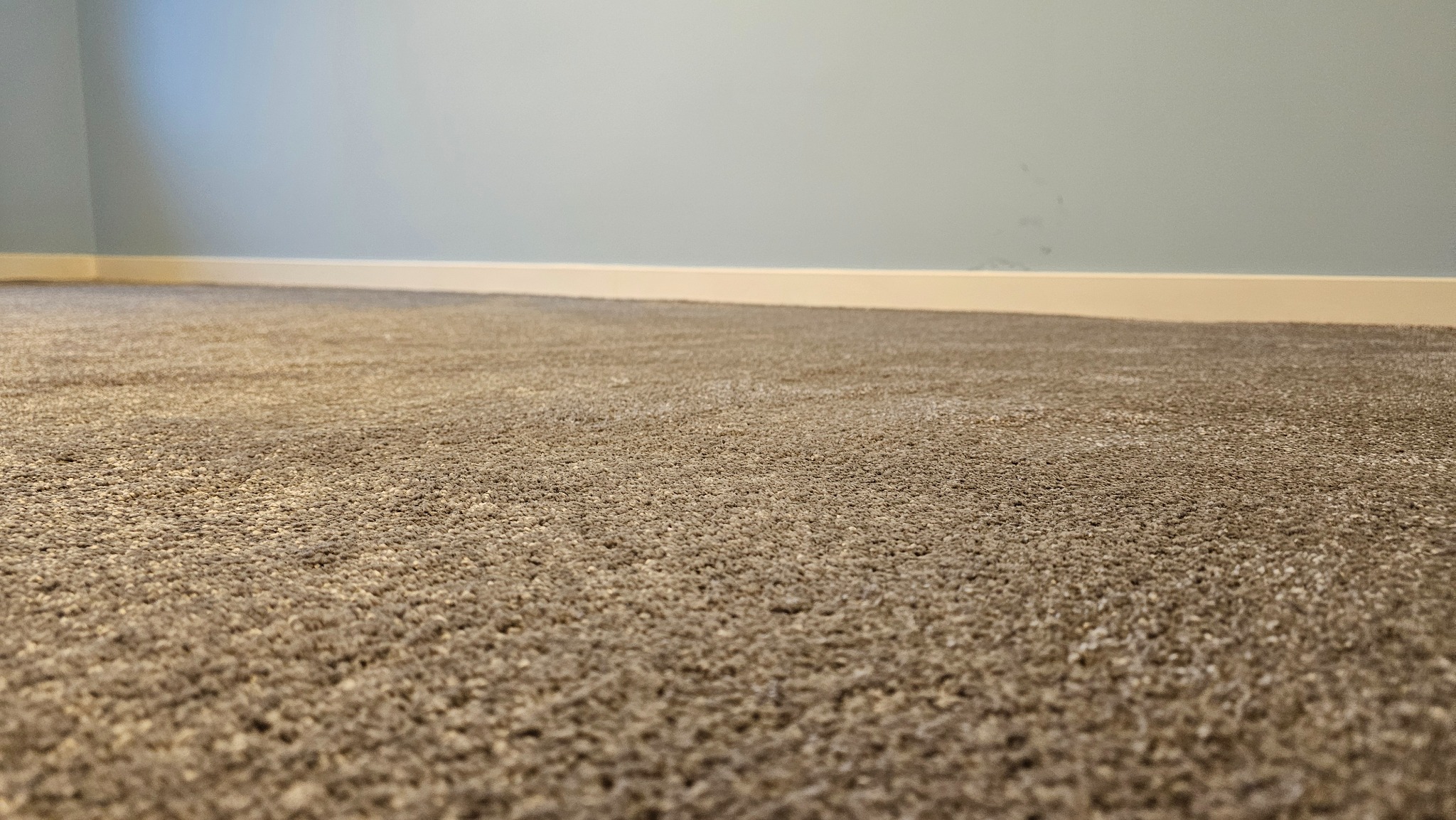 Beżowa wykładzina dywanowa w pokoju z błękitnymi ścianami i białą listwą przypodłogową, ujęcie z niskiej perspektywy, ukazujące fakturę materiału.