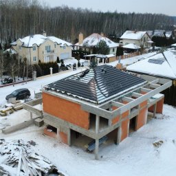 Stan surowy otwarty domu z częściowo położonym dachem w zimowej scenerii Piaseczna. Widoczne bloczki silikatowe i betonowe elementy konstrukcyjne.