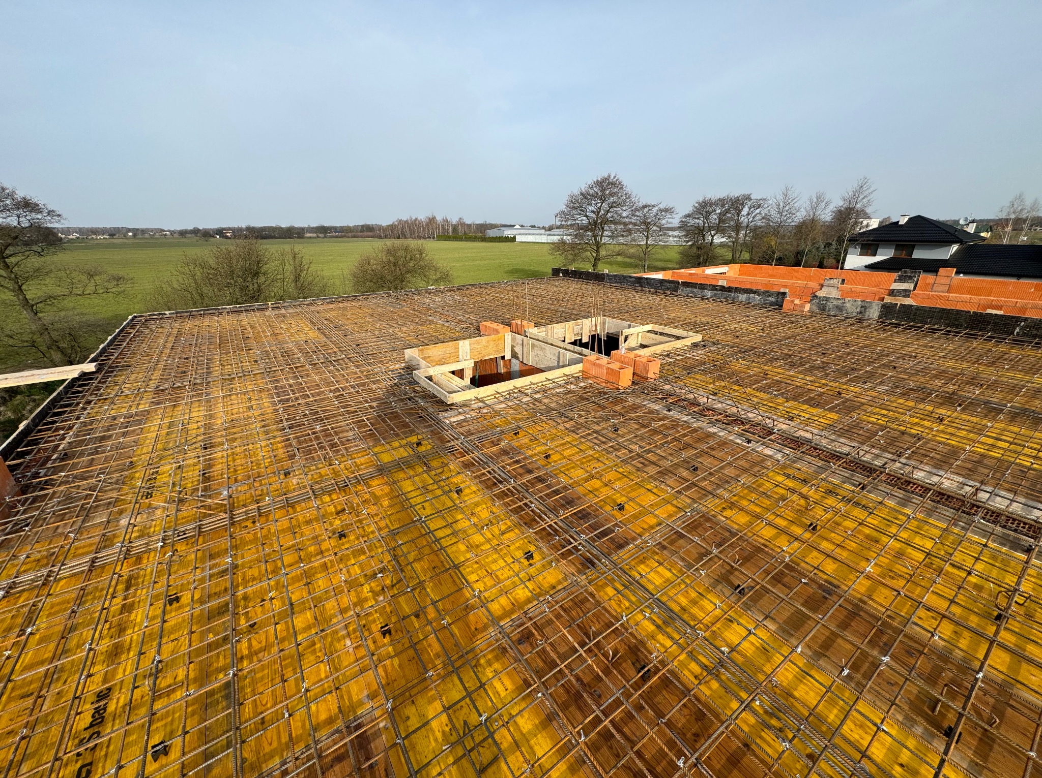 Zbrojenie stropu na żółtym szalunku, przygotowane do zalania betonem na budowie domu w Piasecznie, widok z góry na konstrukcję z otworami na schody lub komin.