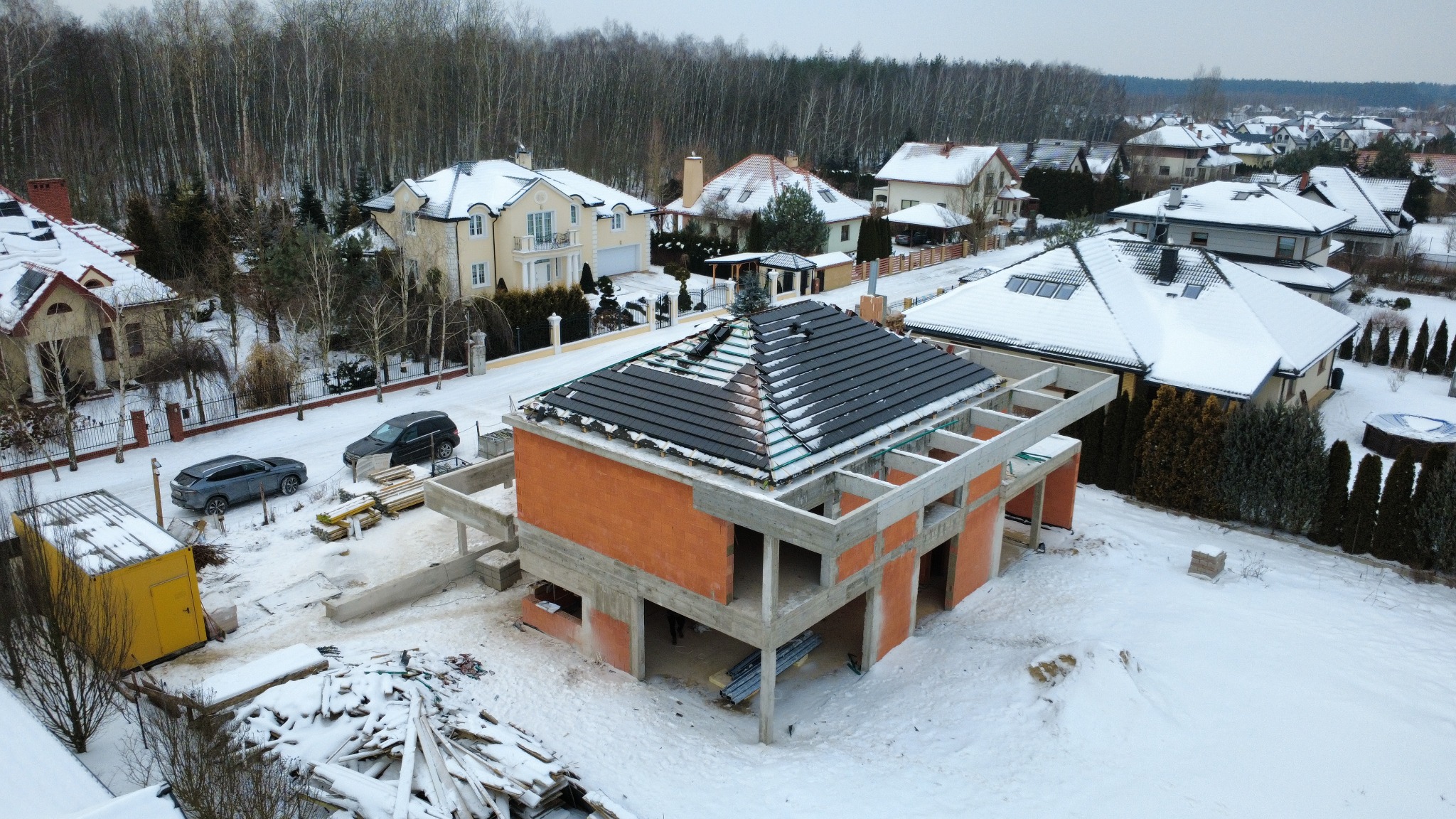 Stan surowy otwarty domu z częściowo położonym dachem w zimowej scenerii Piaseczna. Widoczne bloczki silikatowe i betonowe elementy konstrukcyjne.