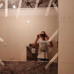 Mateusz nie - Zamontowane lustro w łazience, zabezpieczone taśmą malarską, odbicie osoby robiącej zdjęcie telefonem.