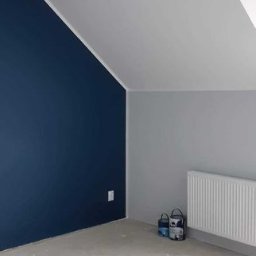 Mateusz nie - Pomalowane na granatowo i szaro poddasze ze skosami, widoczne puszki farby i grzejnik.