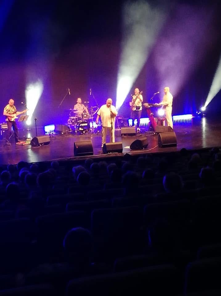 Zespół muzyczny na scenie podczas występu, oświetlony reflektorami, widok z widowni.