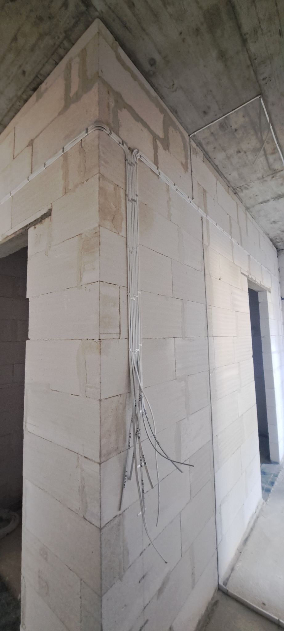 Surowe wnętrze w trakcie prac: kable elektryczne poprowadzone po ścianach z betonu komórkowego, widoczne otwarte końcówki przewodów i fragment sufitu.