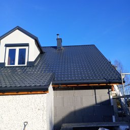 Grzegorz ziolkowski - Nowy, ciemnoszary dach z blachodachówki modułowej na domu w trakcie budowy, widoczne orynnowanie, komin i fragment rusztowania.