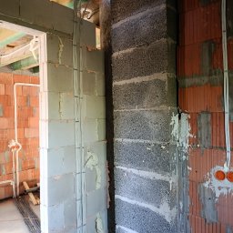 Marcin - Wnętrze budynku w stanie surowym z widocznymi instalacjami elektrycznymi: ułożone przewody w peszlach na ścianach z cegły i bloczków betonowych, puszki instalacyjne, niebieskie rury pod drewnianym...