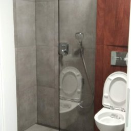 Gabbud - Nowoczesna łazienka z kabiną prysznicową typu walk-in, wykończona szarymi płytkami, z widoczną toaletą wiszącą i drewnianą zabudową.