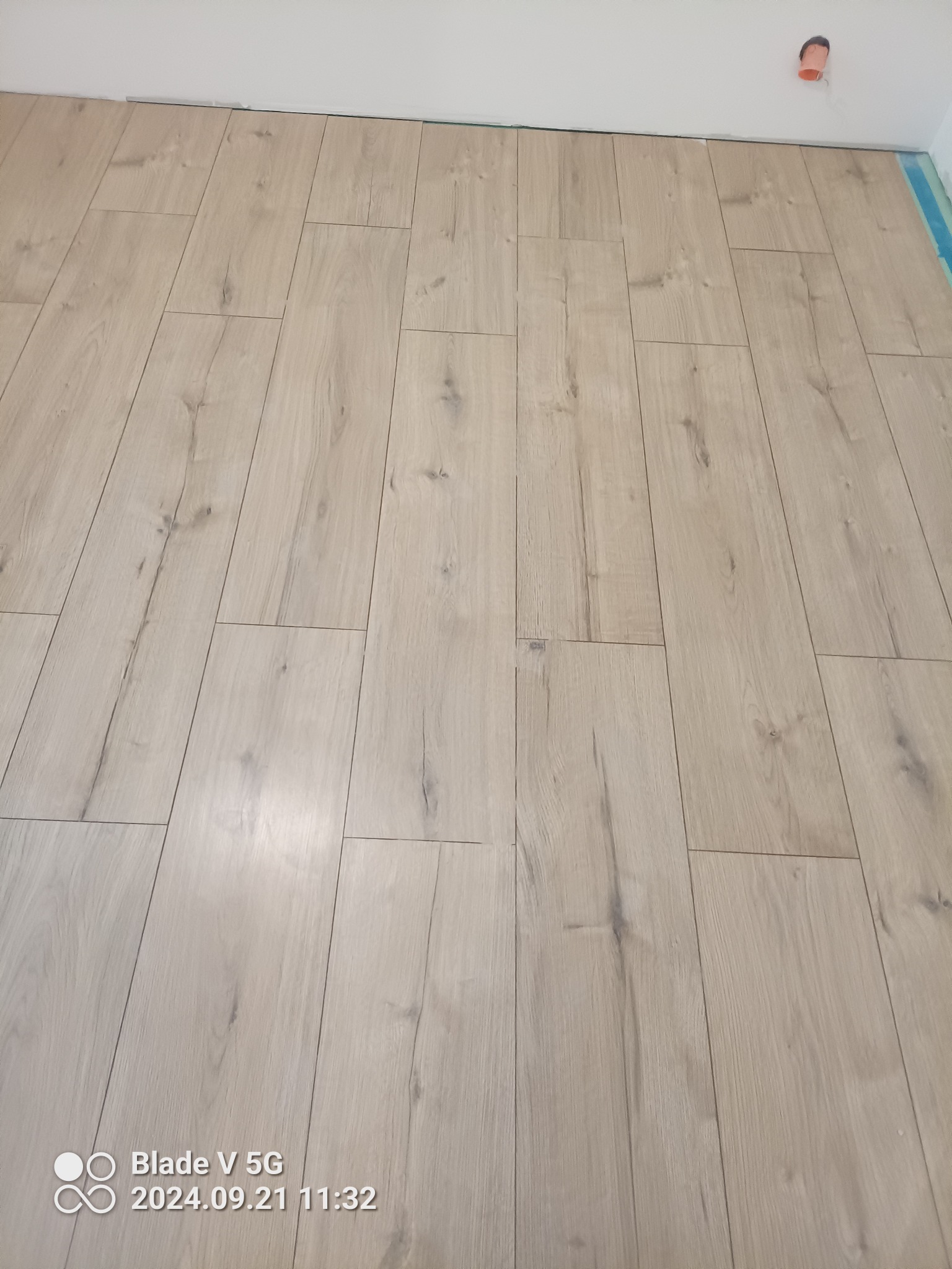 Ułożone panele podłogowe w jasnym odcieniu drewna, widoczna listwa przypodłogowa i fragment instalacji elektrycznej na suficie.