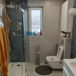 Jasna łazienka z kabiną prysznicową typu walk-in, szarą mozaiką i marmurowymi płytkami. Widoczne okno z widokiem na zimowy krajobraz. Nowoczesny design.