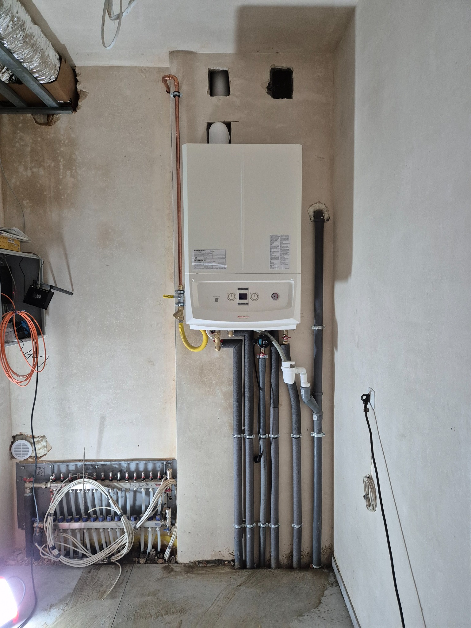 Nowy, wiszący piec gazowy marki Viessmann, z podłączeniem do instalacji grzewczej i pionowymi rurami, zamontowany na surowej ścianie w trakcie prac wykończeniowych.