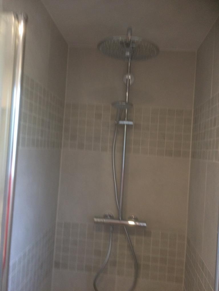 Kabina prysznicowa z deszczownicą i baterią termostatyczną, wykończona płytkami w odcieniach beżu i szarości z delikatnym wzorem mozaiki.