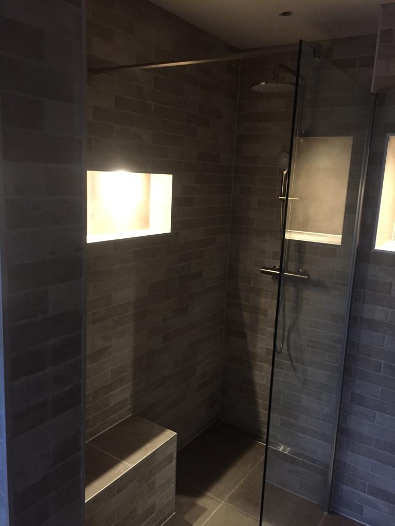 Nowoczesna kabina prysznicowa z szarymi cegiełkami, wbudowaną półką podświetloną od wewnątrz i szklaną ścianką.