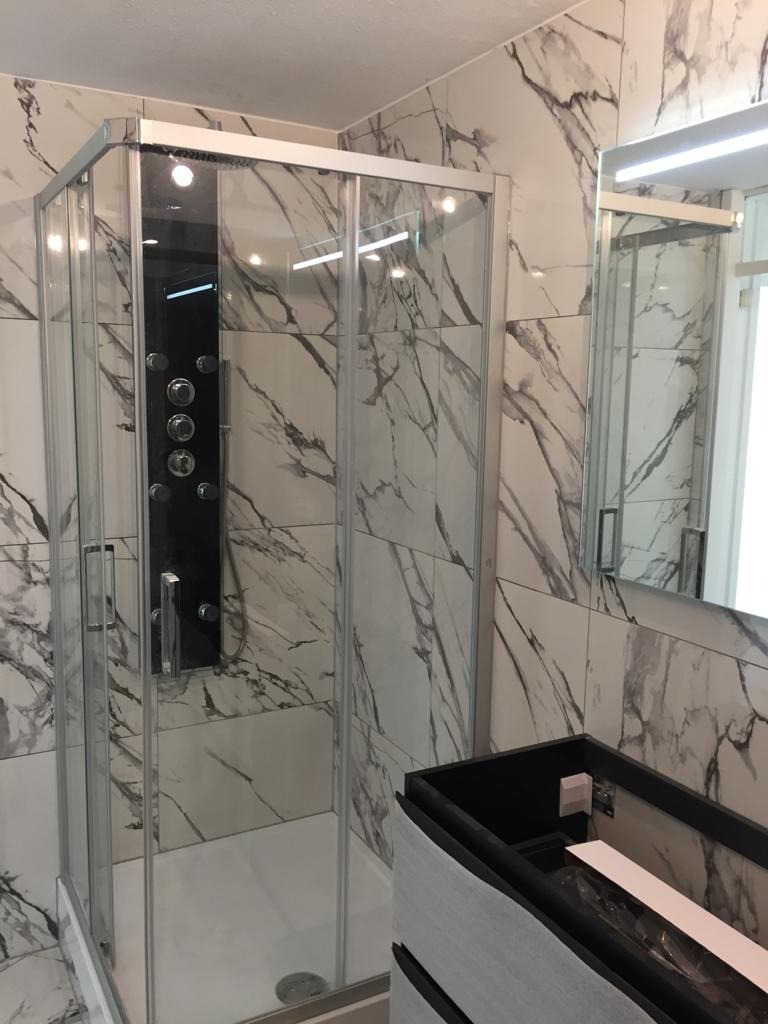 Wykończona łazienka z kabiną prysznicową z hydromasażem, marmurowe płytki na ścianach i umywalka z szafką podwieszaną.