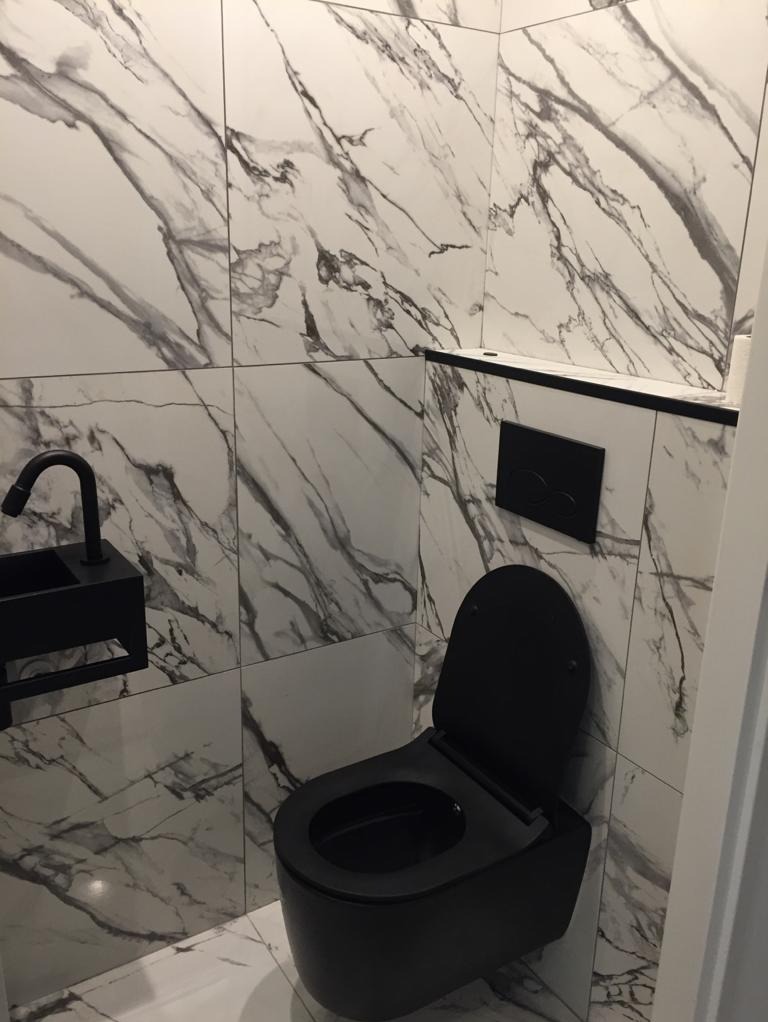 Nowoczesna łazienka z czarną armaturą i misą WC oraz białymi płytkami imitującymi marmur.