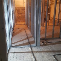 Adrian Antas - Wnętrze w trakcie montażu ścian działowych z profili stalowych, widoczne przewody instalacyjne na podłodze i drewniana konstrukcja stropu.