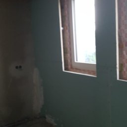 Adrian Antas - Wnętrze w trakcie montażu płyt kartonowo-gipsowych przy oknie, widoczne szpachlowane łączenia i surowy strop z izolacją.