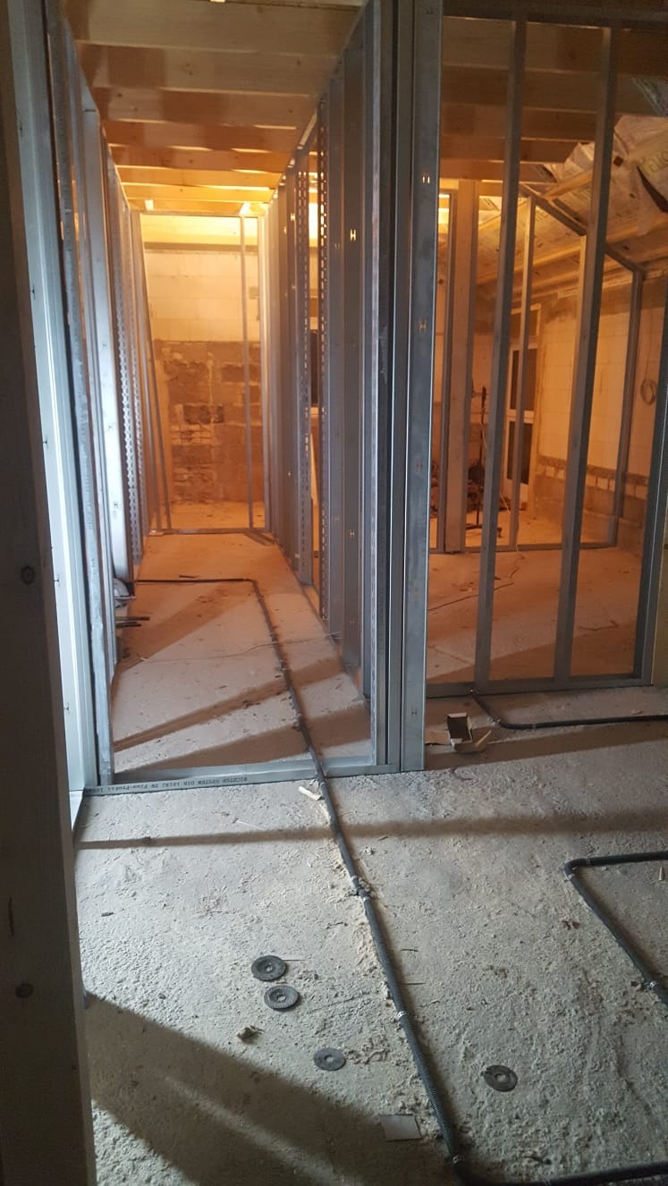 Montaż metalowej konstrukcji ścian działowych z płyt karton gips na surowym betonowym podłożu, widoczne przewody instalacyjne i tarcze do szlifierki.