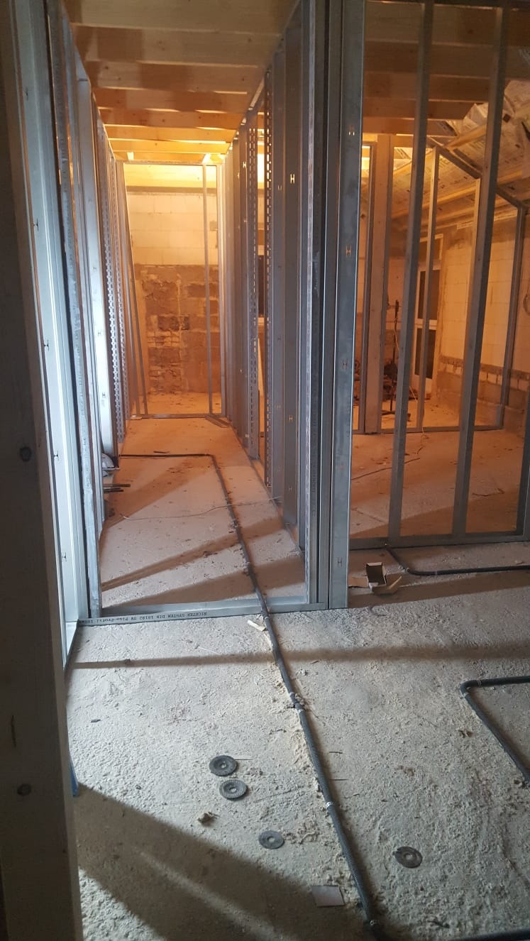 Wnętrze w trakcie montażu ścian działowych z profili stalowych, widoczne przewody instalacyjne na podłodze i drewniana konstrukcja stropu.